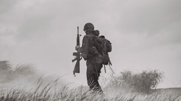 grayscale photo of man in black jacket and pants holding rifle