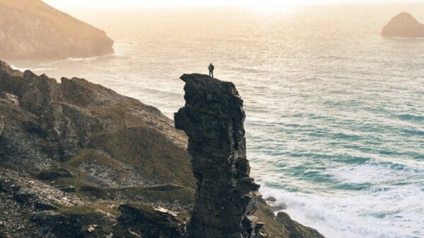 man standing on rock cliff near body of water
