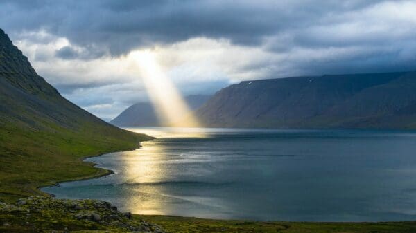 sun reflection on calm water near green mountains