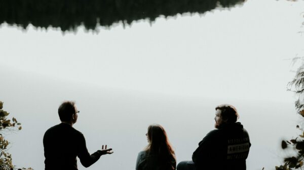 silhouette of three people sitting on cliff under foggy weather