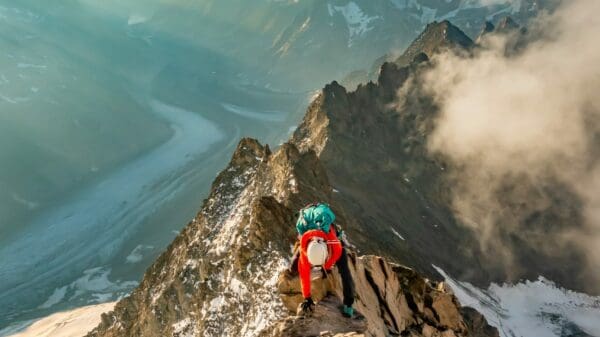 man in red jacket and blue denim jeans standing on rock formation during daytime
